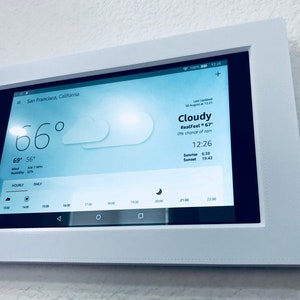 May include: A white tablet mounted on a wall displays a weather forecast for San Francisco, California. The current temperature is 66 degrees Fahrenheit, with a real feel of 67 degrees. The forecast is cloudy with a 0% chance of rain. The time is 12:26 PM. The sunrise is at 6:30 AM and the sunset is at 7:42 PM.