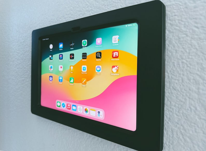 May include: A black wall mount frame with a tablet inside. The tablet screen displays a variety of colorful app icons on a pink and yellow background.