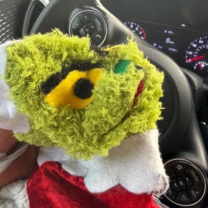 Può includere: Una calza di Natale in peluche con la faccia verde e pelosa del Grinch con un occhio giallo, dettagli neri e una bocca rossa. La calza ha un corpo in velluto rosso con un bordo bianco.