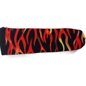 May include: A black fabric sleeve with a flame pattern in red, orange, and yellow. The sleeve is rectangular with rounded ends and is likely designed to protect an item.