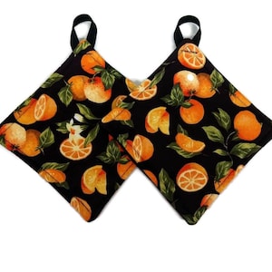 May include: A pair of black pot holders with a pattern of orange slices and green leaves.
