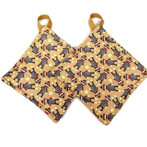 Op de afbeelding: Een paar beige ovenwanten met een patroon van grijze sokpoppen en rode knopen.