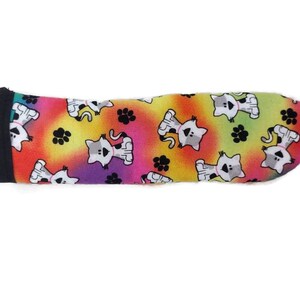 May include: A colourful fabric sleeve with a repeating pattern of white cats and black paw prints on a rainbow background.