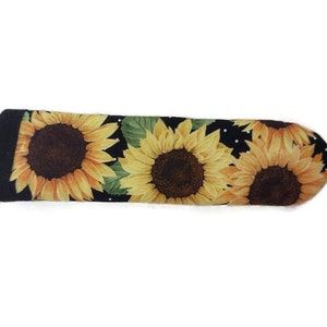 May include: Black fabric pot holder with a sunflower pattern. The pot holder has white polka dots and a black border.