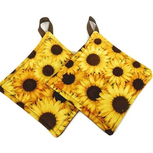 Può includere: Un paio di presine marroni e gialle con un motivo a girasole. Le presine sono fatte di tessuto e hanno un'ansa a forma di anello.