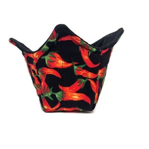 Puede incluir: Un bol de tela negro con estampado de chiles rojos. El bol está doblado y tiene una abertura en forma de estrella.