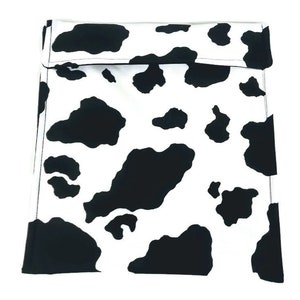 May include: A black and white cow print reusable sandwich bag. The bag has a flap that folds over and secures with a velcro closure.