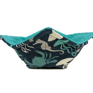 May include: A fabric bowl with a dark blue exterior featuring a sea life pattern of seahorses, crabs, and seaweed in shades of teal and white. The interior is a solid teal color.