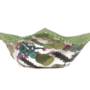 May include: A green and white fabric bowl with a cactus print. The bowl is folded and has a white polka dot pattern on the outside.