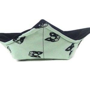 May include: A light green fabric bowl with a black and white dog print. The bowl is folded and has a black fabric lining.