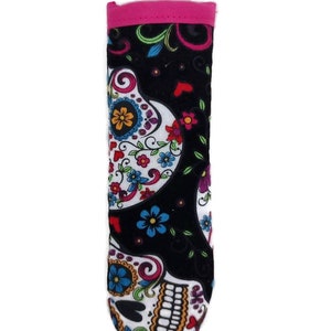 Puede incluir: Un estuche de tela para gafas con un diseño de calavera de azúcar del Día de Muertos. El estuche tiene un fondo negro con detalles florales y de calaveras coloridos. El borde superior es rosa brillante.