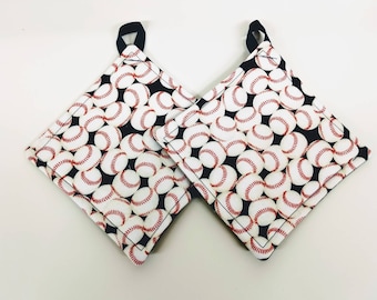 May include: Two black and white pot holders with a baseball pattern. The pot holders have a black border and a black loop for hanging.