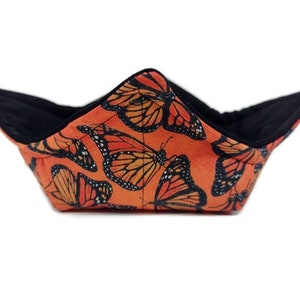 May include: A black and orange fabric bowl with a butterfly pattern. The bowl is folded into a shape that resembles a boat.
