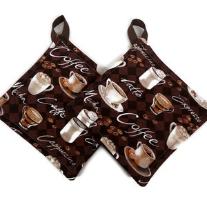 May include: Two brown quilted pot holders with a coffee theme. The pot holders feature a checkered pattern with coffee beans and various coffee drinks, including cappuccino, latte, mocha, espresso, and coffee. The text "Coffee" is written on both pot holders.