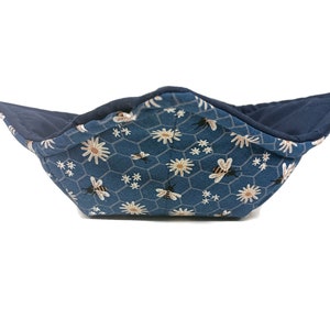 May include: A blue fabric bowl with a honeycomb and bee pattern. The bowl is lined with a dark blue fabric.