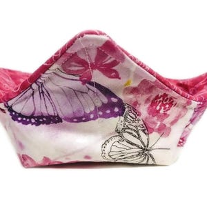 May include: A pink and white fabric bowl with a butterfly print. The bowl is folded into a star shape.