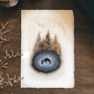 Könnte beinhalten: Aquarellmalerei auf strukturiertem Papier mit einem dunkelblauen und schwarzen Oval mit einer Halbmondform im Inneren. Goldene Flocken und goldfarbene Bäume befinden sich über dem Oval. Das Papier hat einen Büttenrand.