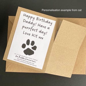 May include: A brown card with a white insert. The insert reads "Happy Birthday Daddy! Have a purrfect day! Love Kit xxx" with a paw print. The card is open, revealing a blank insert. Text at the bottom reads "Art & Crafts Handmade in Devon, England".
