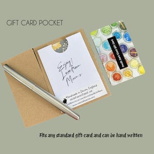 Pu&ograve; includere: Una tasca per biglietti regalo in cartoncino marrone, con una carta bianca all'interno con testo scritto a mano e una penna d'argento. Una carta regalo colorata &egrave; accanto alla tasca. Il testo recita "Enjoy! Love from Mum x".