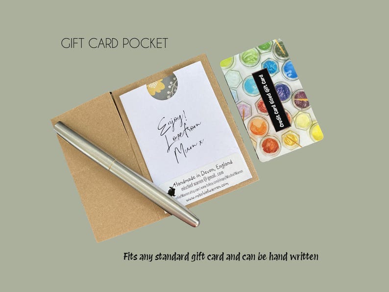 Pu&ograve; includere: Una tasca per biglietti regalo in cartoncino marrone, con una carta bianca all'interno con testo scritto a mano e una penna d'argento. Una carta regalo colorata &egrave; accanto alla tasca. Il testo recita "Enjoy! Love from Mum x".