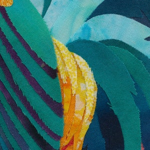 Op de afbeelding: Close-up van een kleurrijk kunstwerk van stof met een mix van turquoise, blauw, geel en oranje stof. De stof is in verschillende vormen geknipt en aan elkaar genaaid om een ​​getextureerd en abstract ontwerp te cre&euml;ren.