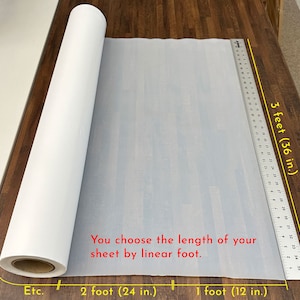 May include: A white roll of paper on a wooden surface. The paper is 3 feet wide and can be cut to any length. The text on the image reads: "You choose the length of your sheet by linear foot.  Etc. 2 foot (24 in.) 1 foot (12 in.)"