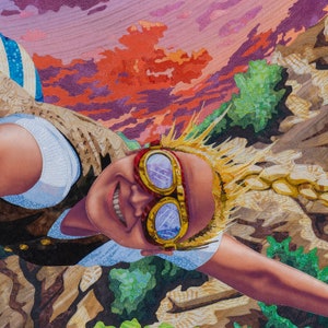 May include: A young person with blonde hair wearing goggles and a vest, smiling and looking up at the sky. The background is a colorful sunset with clouds.