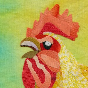 Op de afbeelding: Close-up van een haanenkopp gemaakt van stofresten. De kam van de haan is rood, de snavel is bruin en het oog is zwart. De achtergrond is een gele en groene gradi&euml;nt.