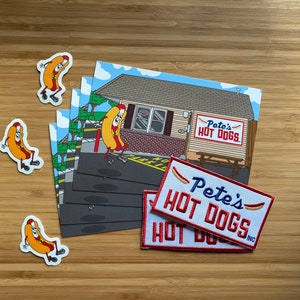May include: A set of four hot dog character stickers and two embroidered patches with the text "Pete's Hot Dogs" in red and blue. The stickers are yellow and red with black outlines. The patches are white with red and blue embroidery.