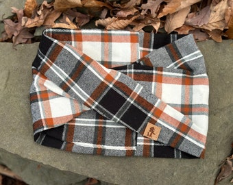 May include: A black, white and orange plaid fabric dog collar with a small brown leather patch featuring a tree logo.