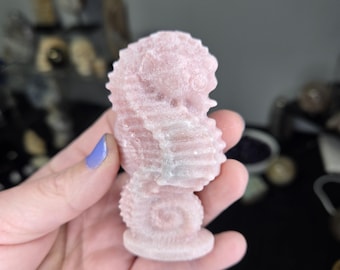 May include: A pink and white seahorse-shaped crystal carving. The carving is detailed and intricate, with a textured surface.