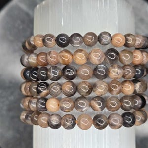 May include: A stack of six bracelets made with sunstone beads. The beads are a mix of brown, black, and white.