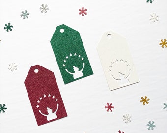 May include: Three gift tags with a snowman design. The tags are green, red, and white with glitter. Each tag has a circle of stars around the snowman.