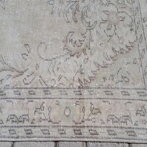 May include: A vintage rug with a faded floral pattern in shades of beige and brown. The rug has a distressed look and a fringe border.