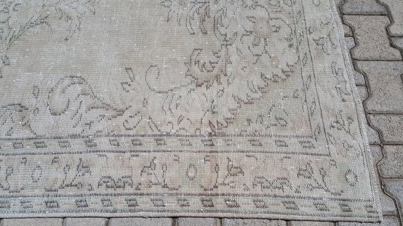May include: A vintage rug with a faded floral pattern in shades of beige and brown. The rug has a distressed look and a fringe border.