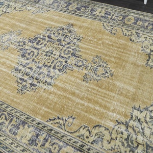May include: A vintage-style rug with a faded gold background and a blue and white floral pattern. The rug has a distressed look and a fringed edge.