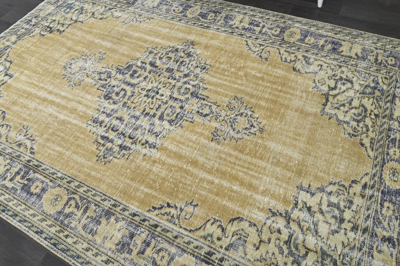 May include: A vintage-style rug with a faded gold background and a blue and white floral pattern. The rug has a distressed look and a fringed edge.