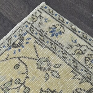 May include: A beige rug with a floral pattern in shades of gray and blue. The rug has a fringed edge.