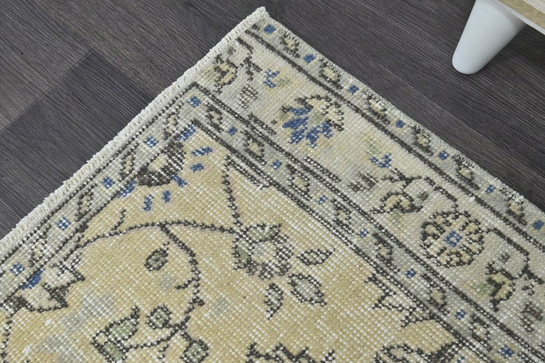 May include: A beige rug with a floral pattern in shades of gray and blue. The rug has a fringed edge.