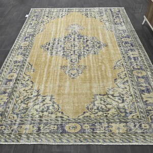 May include: A vintage-style rug with a faded, light brown background and a blue and white floral pattern. The rug has a distressed look and a fringed edge.