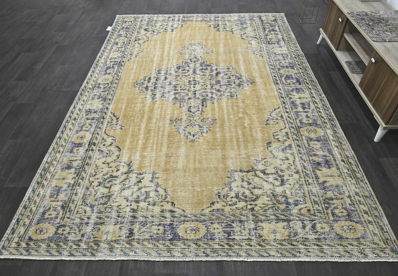May include: A vintage-style rug with a faded, light brown background and a blue and white floral pattern. The rug has a distressed look and a fringed edge.