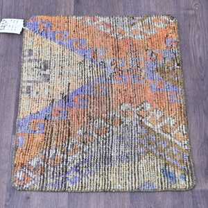 Op de afbeelding: Een klein, rechthoekig tapijt met een geometrisch patroon in tinten oranje, blauw en beige. Het tapijt heeft een verweerde, vintage uitstraling.