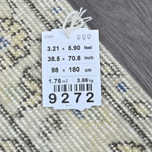 May include: A white tag with black text and a barcode. The tag lists the dimensions of a rug in feet, inches, and centimeters. The rug is 3.21 feet by 5.90 feet, 38.5 inches by 70.8 inches, and 98 centimeters by 180 centimeters. The tag also lists the rug's weight as 3.86 kilograms and its area as 1.76 square meters. The barcode number is 9272.