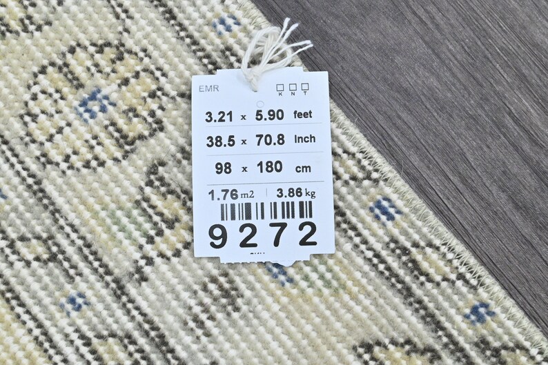 May include: A white tag with black text and a barcode. The tag lists the dimensions of a rug in feet, inches, and centimeters. The rug is 3.21 feet by 5.90 feet, 38.5 inches by 70.8 inches, and 98 centimeters by 180 centimeters. The tag also lists the rug's weight as 3.86 kilograms and its area as 1.76 square meters. The barcode number is 9272.