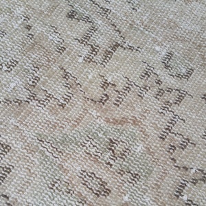 May include: Close-up of a beige and brown woven rug with a geometric pattern. The rug has a distressed look and a soft, textured surface.