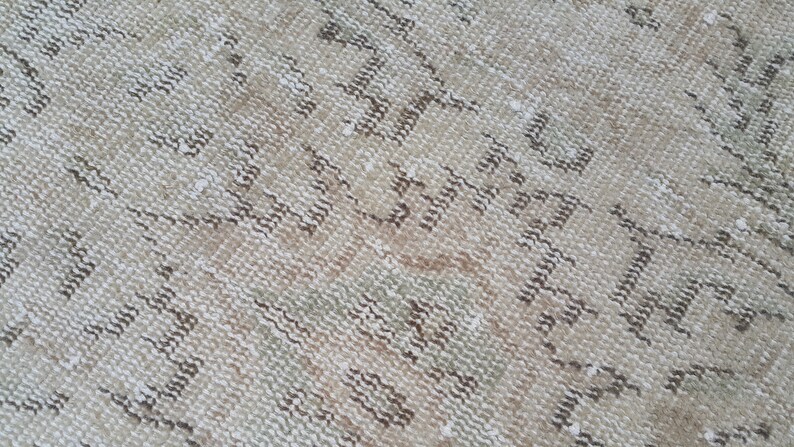 May include: Close-up of a beige and brown woven rug with a geometric pattern. The rug has a distressed look and a soft, textured surface.