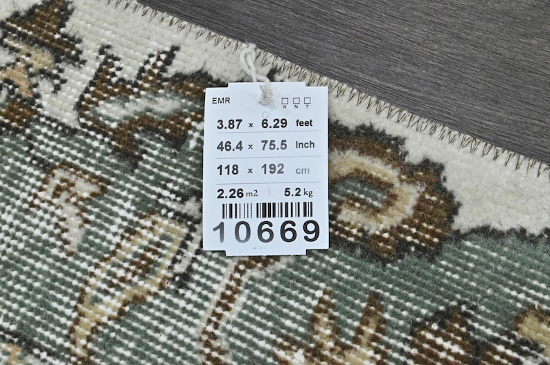 Op de afbeelding: Een wit label met zwarte tekst en een barcode. Het label geeft de afmetingen van een tapijt in voet, inch en centimeter. Het tapijt is 3,87 voet bij 6,29 voet, 46,4 inch bij 75,5 inch en 118 centimeter bij 192 centimeter. Het label geeft ook het gewicht van het tapijt aan, dat 5,2 kilogram is, en de oppervlakte, die 2,26 vierkante meter is. Het barcodenummer is 10669.