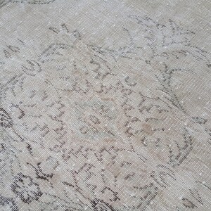 May include: A vintage rug with a faded, light brown background and a pattern of dark brown floral designs. The rug has a worn and distressed look, giving it a rustic and antique feel.