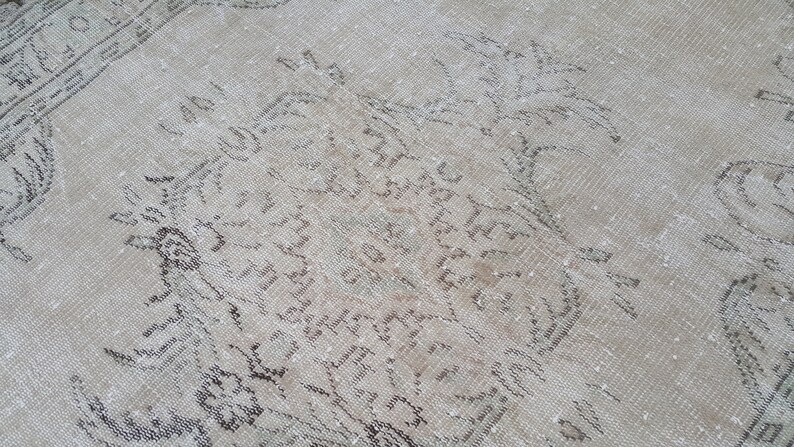May include: A vintage rug with a faded, light brown background and a pattern of dark brown floral designs. The rug has a worn and distressed look, giving it a rustic and antique feel.