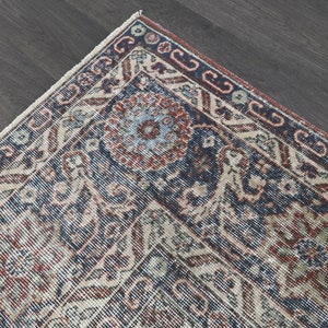 Pode incluir: Close-up de um canto de um tapete vintage com um padr&atilde;o azul, vermelho e creme. O tapete tem um design floral detalhado com detalhes intrincados.
